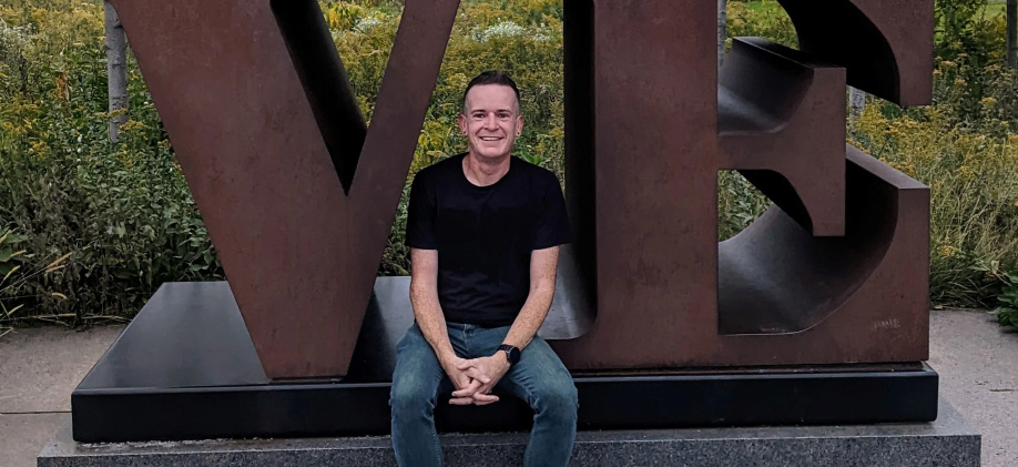 Evan sitting near a sign with the letters 'VE'